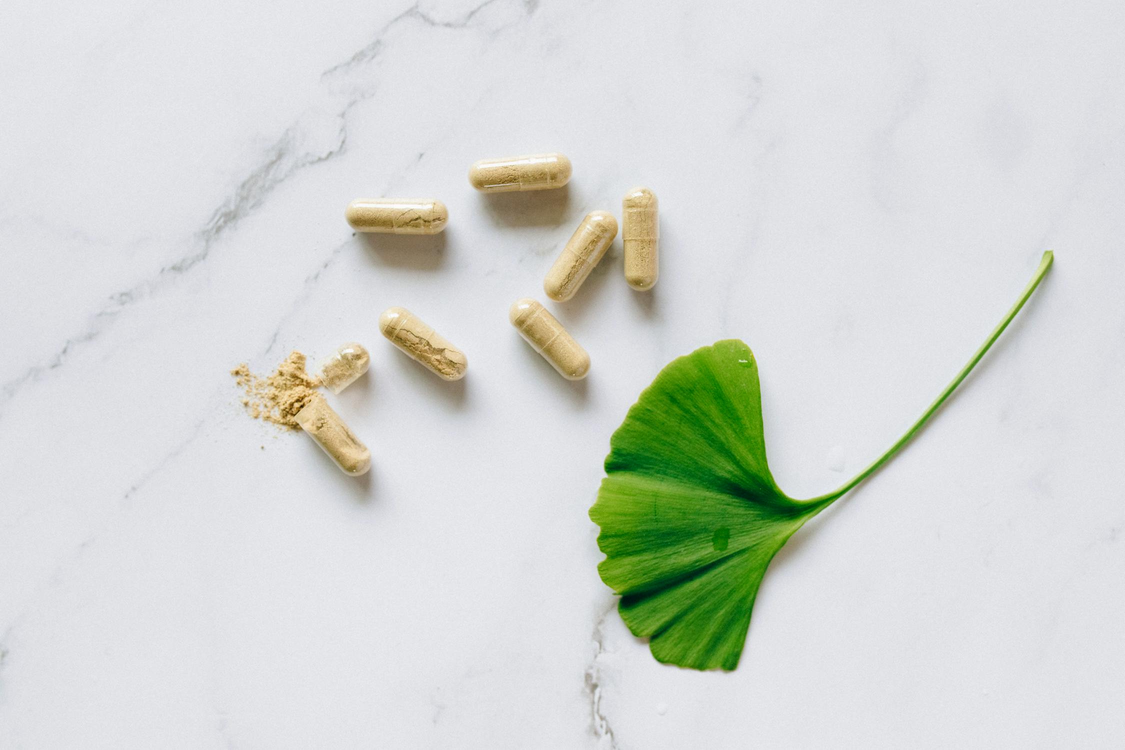 Capsules of a dietary supplement beside a ginkgo leaf on a marble surface, representing anti-cancer supplements and natural health options.