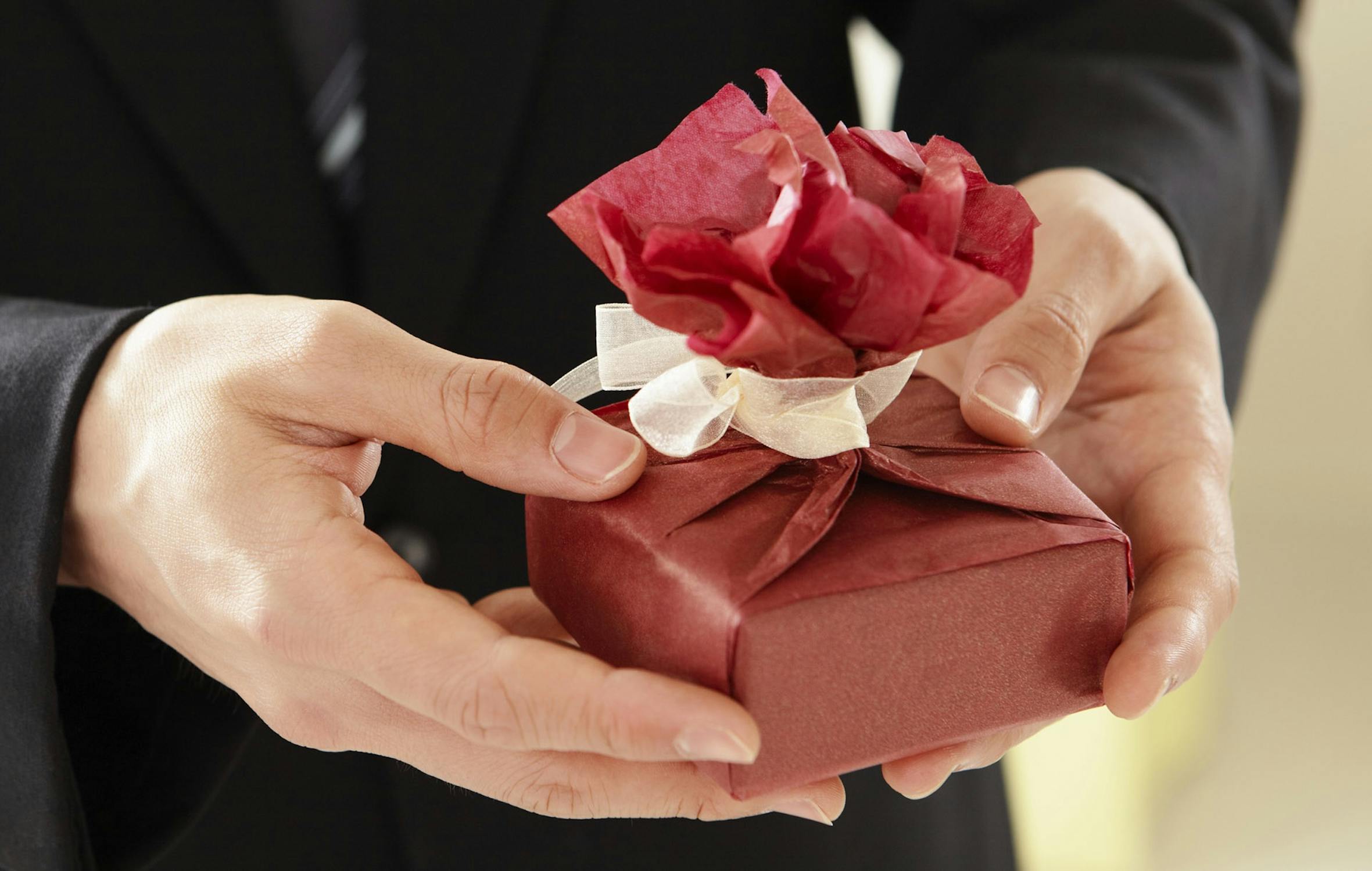 A person holding a neatly wrapped gift with a red ribbon, symbolizing the importance of choosing thoughtful and considerate presents for cancer patients and survivors.