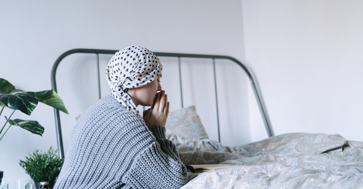 Una persona che indossa un foulard siede su un letto, a simboleggiare il viaggio emotivo e il supporto necessario durante i trattamenti di chemioterapia.