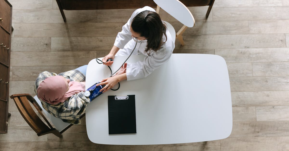 A doctor using a blood pressure cuff to monitor the health of a cancer survivor at a table with a clipboard beside them.