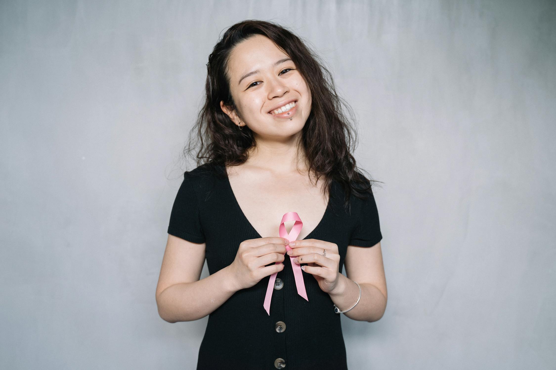 A woman smiling while holding a pink ribbon