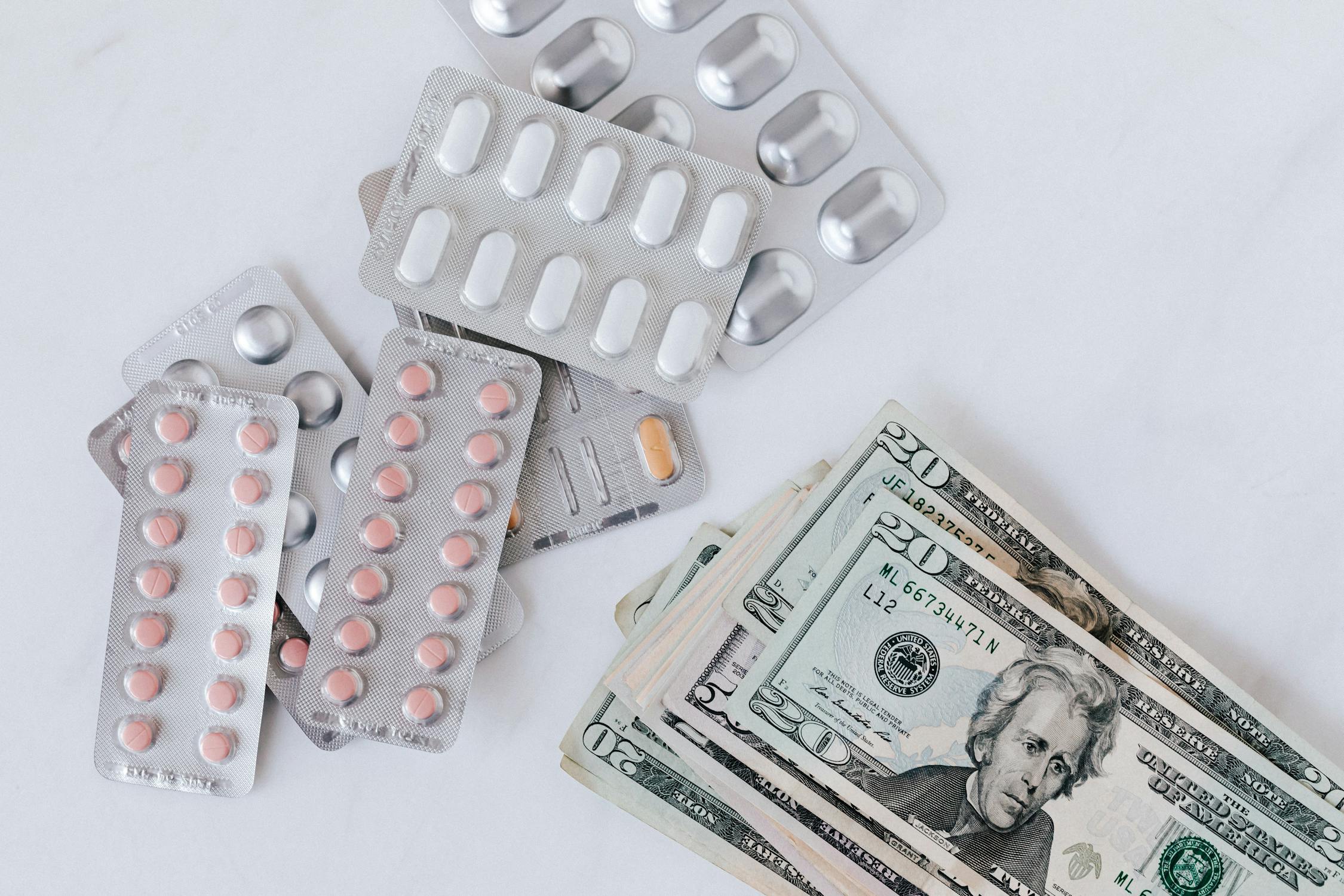 Una colección de blísteres de medicamentos junto a una pila de billetes de dólar, que simbolizan los problemas económicos a los que se enfrentan los enfermos de cáncer.