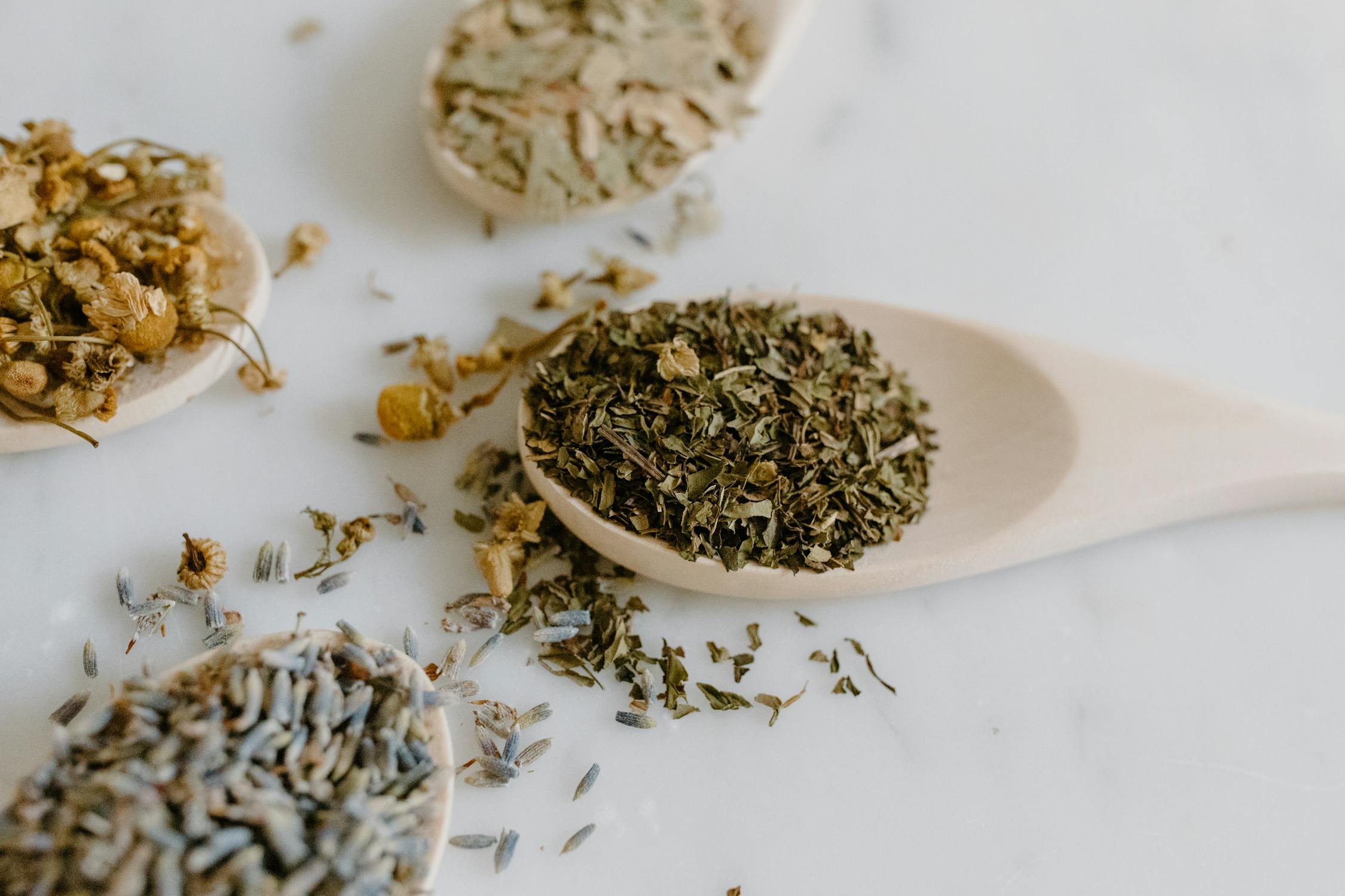 Wooden spoons filled with dried herbs like chamomile and lavender, used for natural scalp care during chemotherapy.