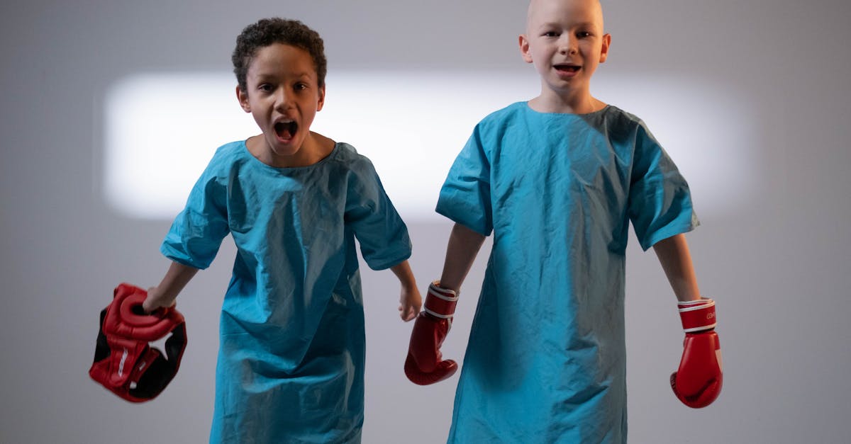 Deux jeunes enfants en blouse d'hôpital, portant des gants de boxe, symbolisant la force et la résilience lors d'un séjour à l'hôpital.