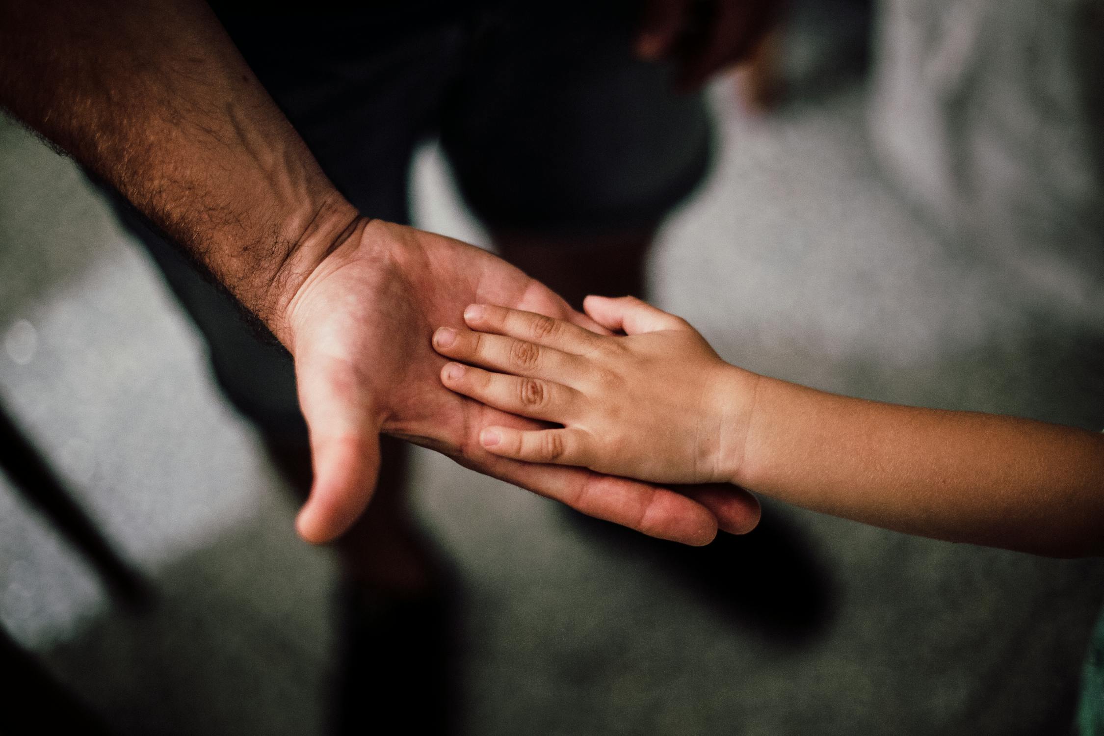Een volwassene en een kind houden elkaars hand vast, als symbool voor steun en zorg voor een kind met kanker.