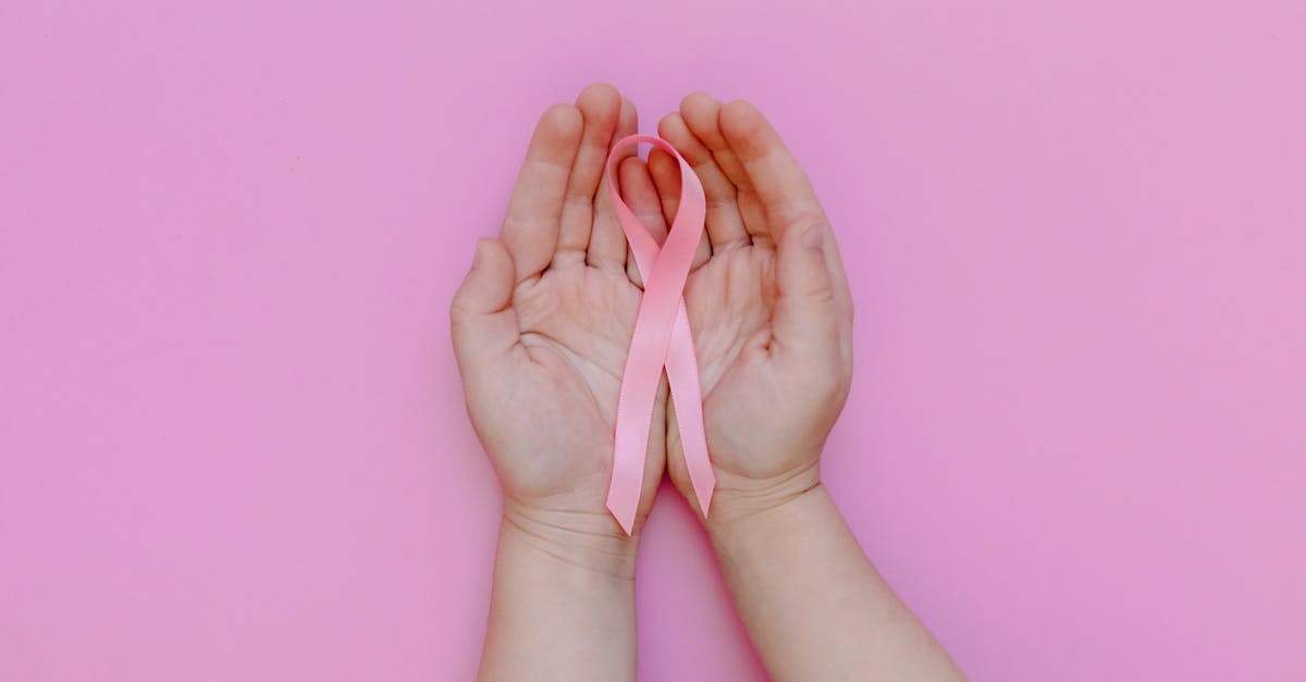 Hands gently holding a pink ribbon on a pink background, representing cancer awareness and the journey of survivors.