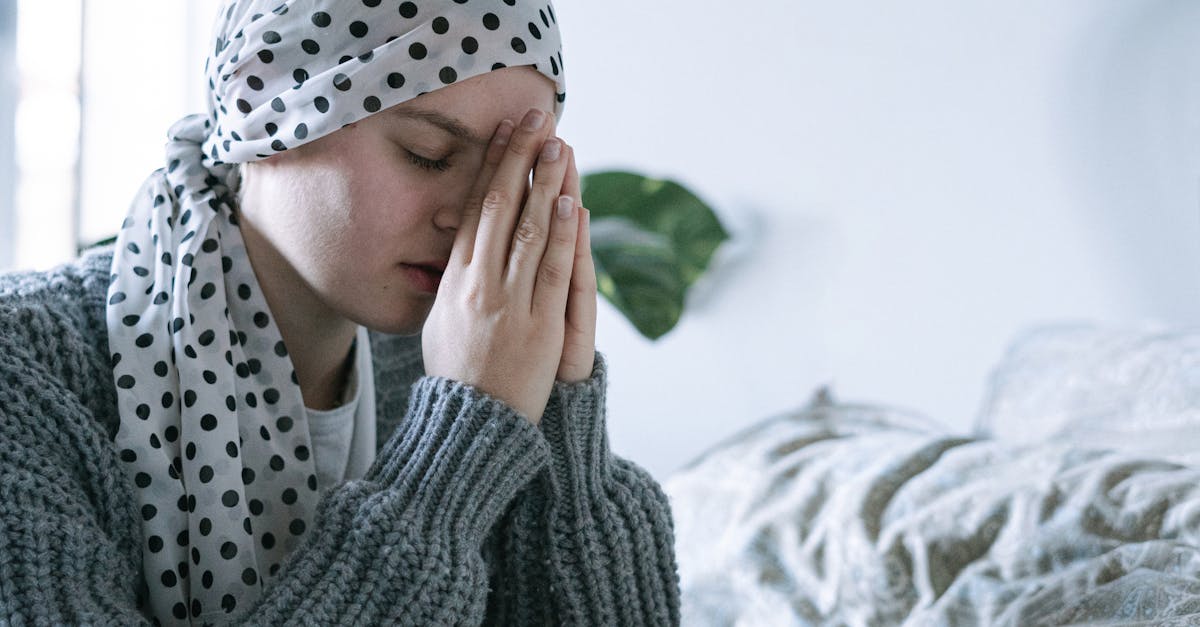A person wearing a headscarf sits with clasped hands, deep in thought, symbolizing resilience and recovery after cancer treatment.