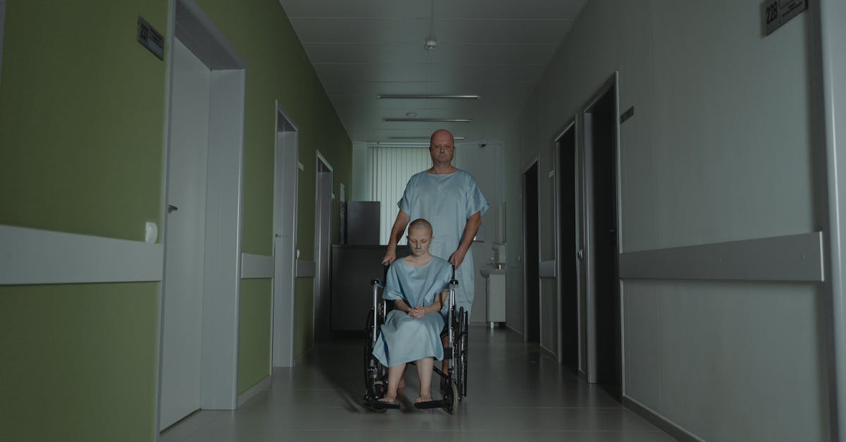 Njegovateljica u bolničkom ogrtaču stoji iza pacijenta u invalidskim kolicima, ilustrirajući usamljenost i emocionalne izazove s kojima se suočava u njezi raka.