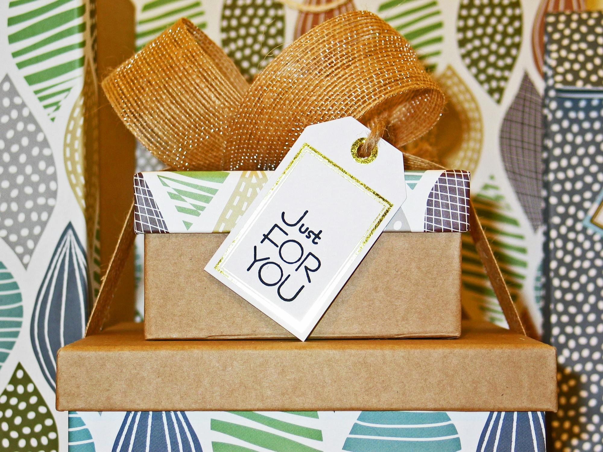 A gift box wrapped in decorative paper with a gold ribbon and a tag reading