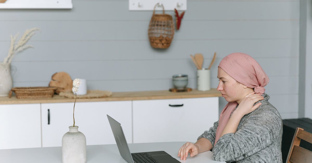 Une femme portant un foulard est assise à une table et utilise un ordinateur portable, ce qui représente une personne susceptible de subir un traitement contre le cancer, mettant en évidence les thèmes de la connexion et de l'empathie.